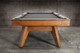 Short wide-angle view of the Doc & Holliday Scholar Slate Pool Table | Full-frame shot showing flared mid-century modern legs, solid maple hardwood frame, and black felt playfield | USA-made luxury billiards table in Heritage Maple finish Short wide-angle view of the Doc & Holliday Scholar Slate Pool Table | Full-frame shot showing flared mid-century modern legs, solid maple hardwood frame, and black felt playfield | USA-made luxury billiards table in Heritage Maple finish